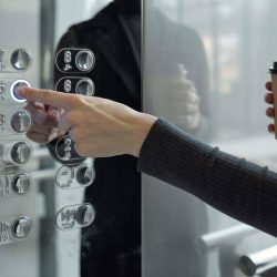 Hand of young businesswoman with drink pushing button inside elevator while going back to office on fifth floor at coffee break